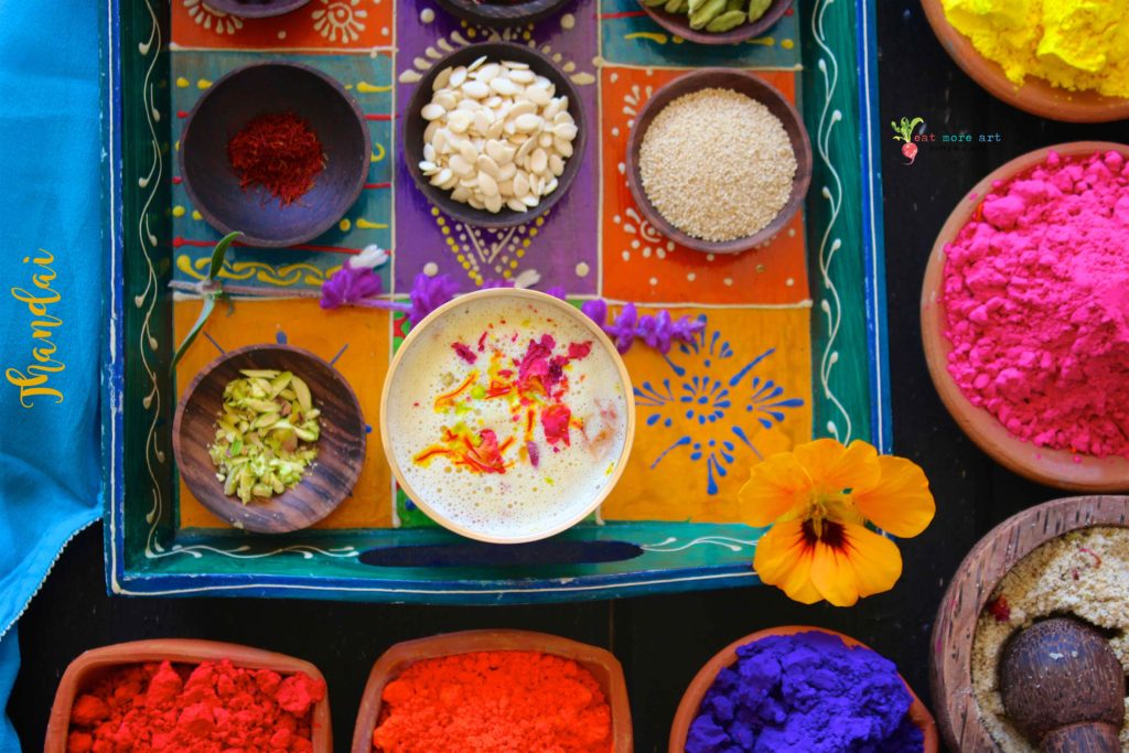 An overhead shot of a colorful tray of thandai, it's ingredients, and holi colors