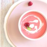 An overhead shot of chilled raspberry dessert soup garnished with mint and heavy cream