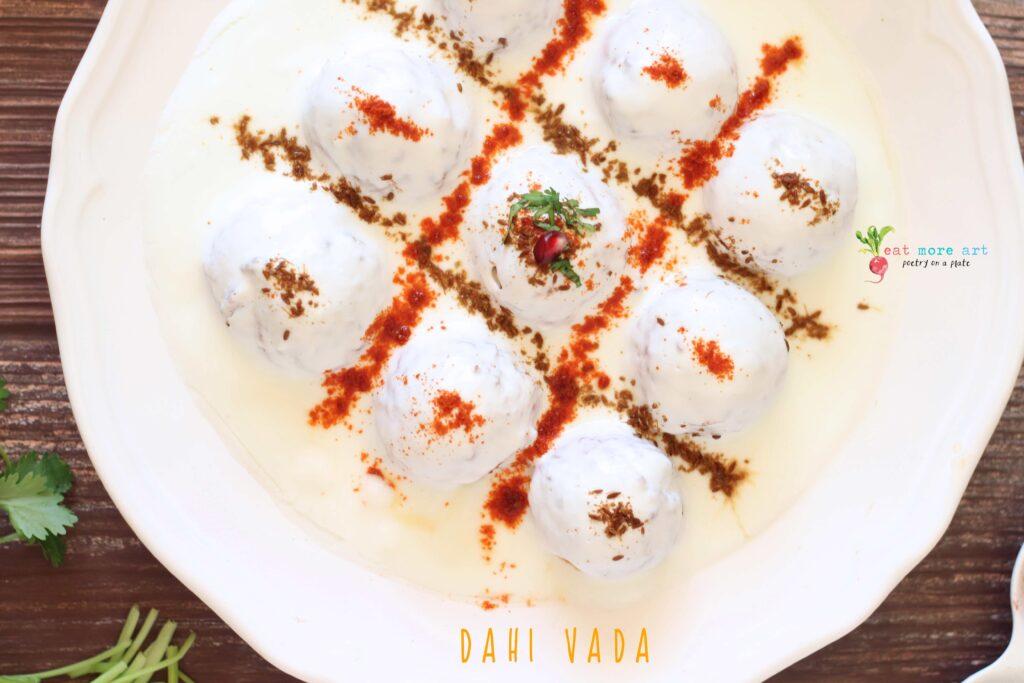 An overhead closeup shot of dahi vada garnished with cumin and chili powder