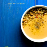 An overhead shot of a bowl of potato lentil soup garnished with pine nuts and oregano