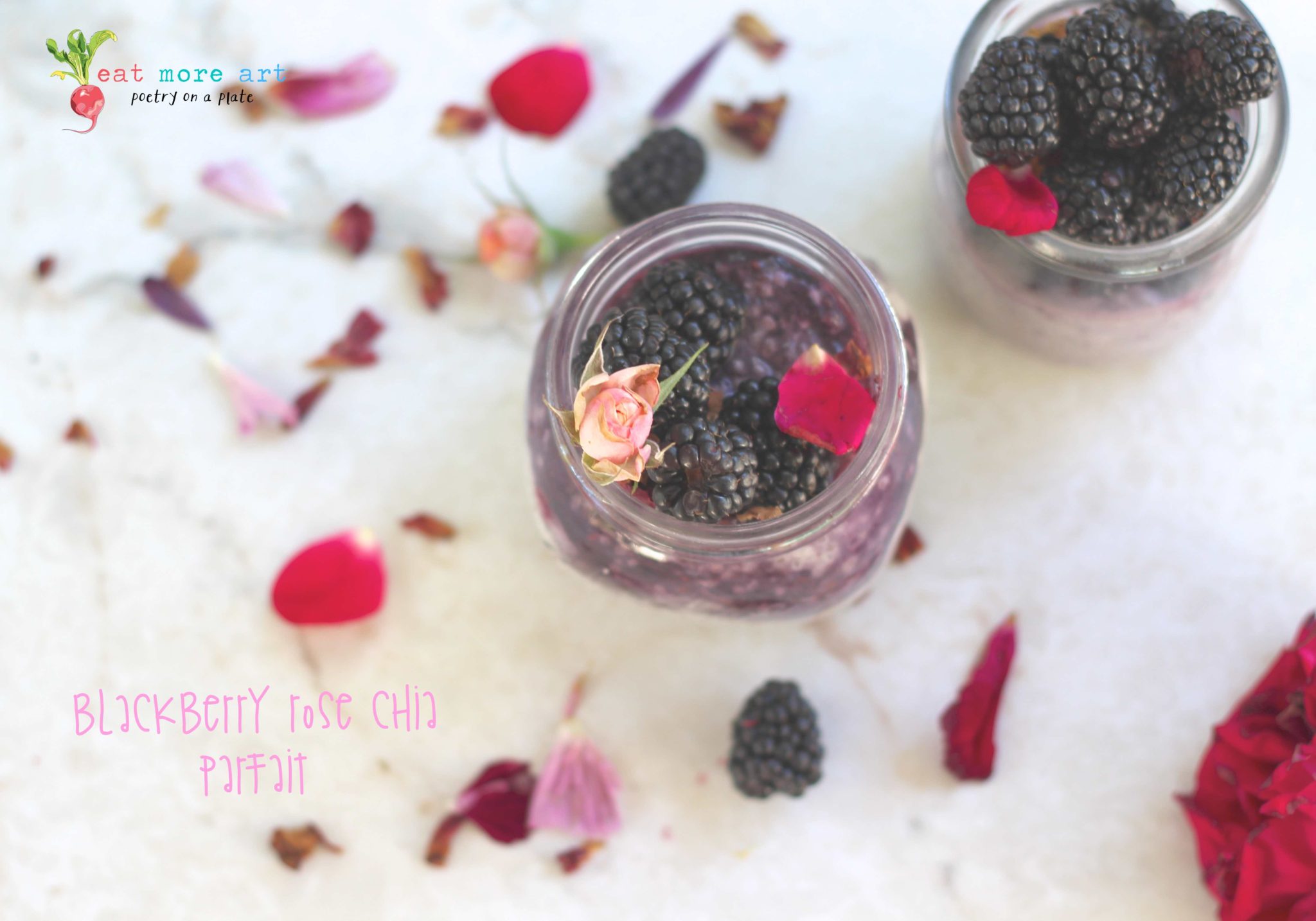 an overhead shot of blackberry rose chia parfait topped with blackberries and rose petals and rose bud on a white backdrop with flower petals and blueberries scattered