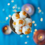 An overhead shot of coconut laddu in a bowl, with teal background and lights with bokeh effect