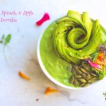 An overhead shot of avocado spinach apple smoothie garnished with avocado rose, edible flowers, and sunflower seeds