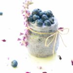 Side shot of a jar of blueberry chia pudding topped with blueberries and garnished with lavender and rose petals on the side