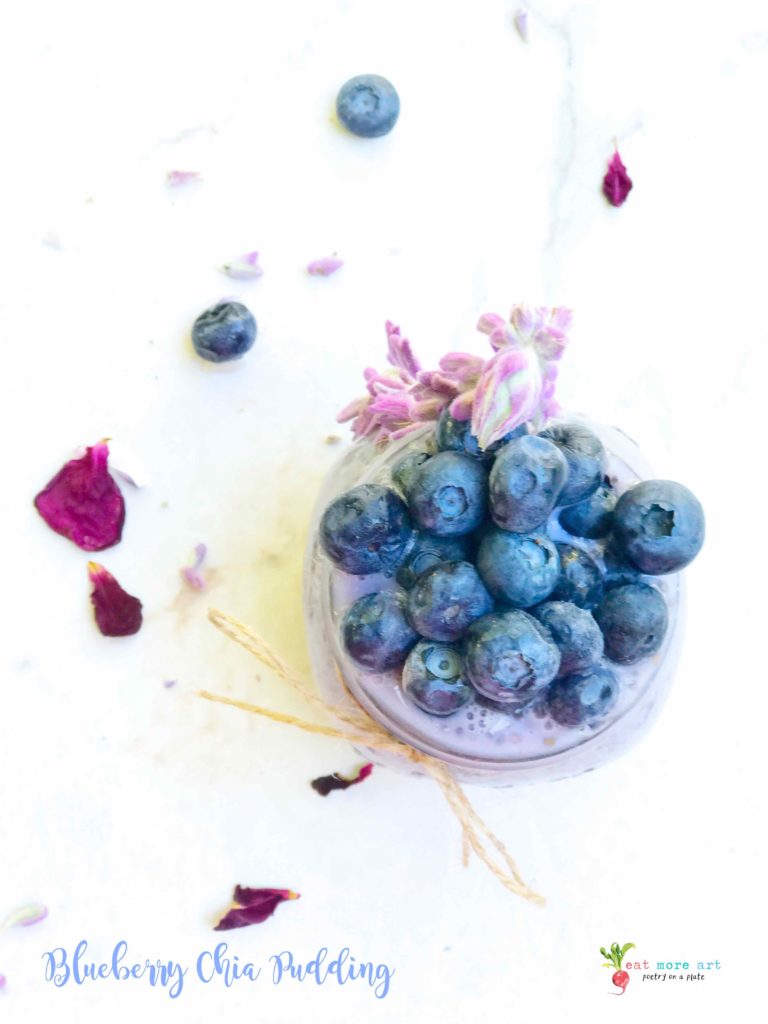 a top shot of a jar of blueberry chia pudding topped with blueberries and garnished with lavender and rose petals on the side