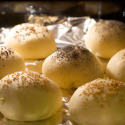 Burger buns topped with poppy seeds and sesame seeds, being baked in the oven